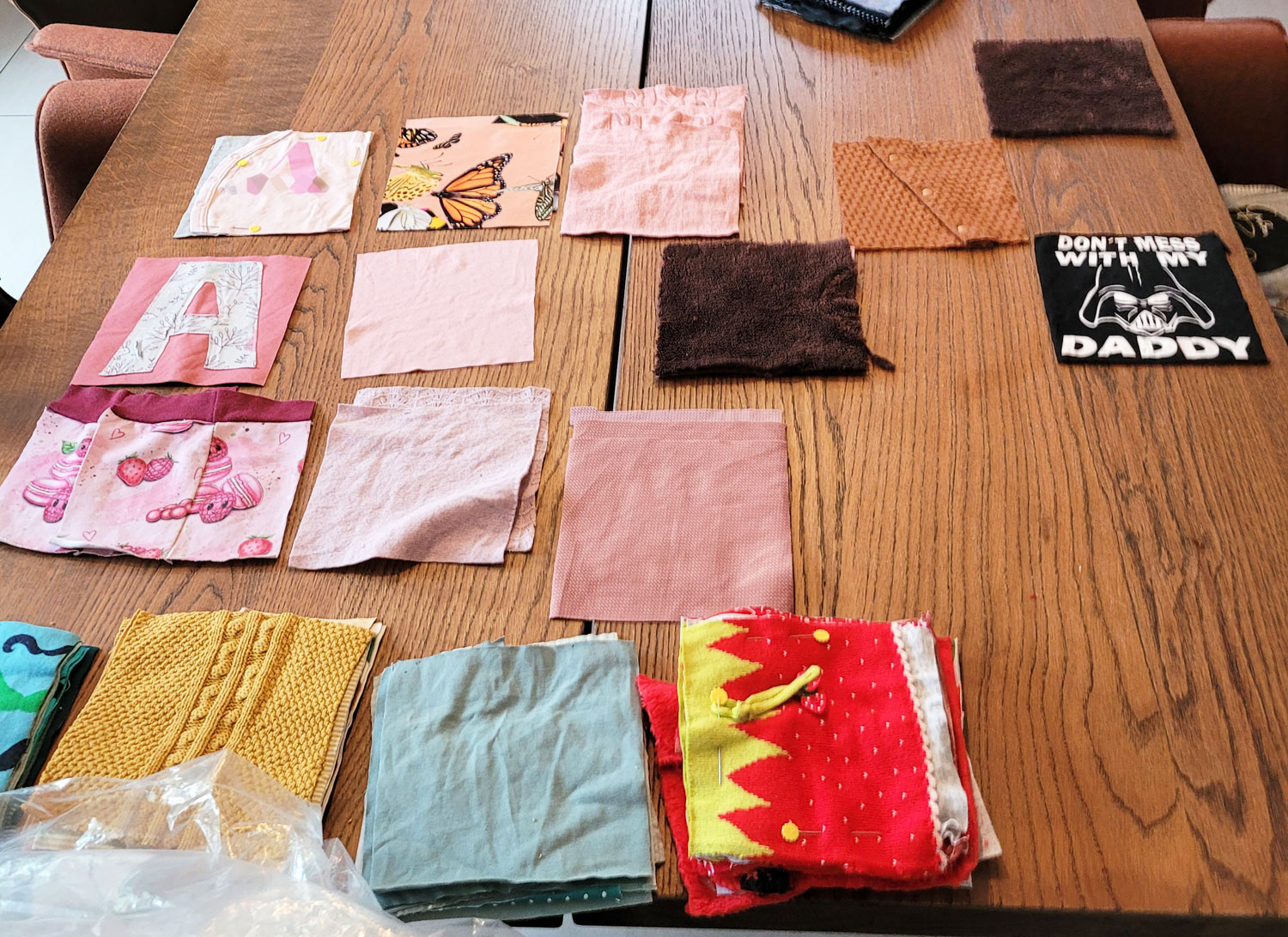 Auf unserem dunkelbraunen Esstisch liegen einige Quadrate ausgebreitet. Rosa ist nach Kleidungsstück nebeneinander ausgelegt. Braune und schwarze Quadrate sind bereits in der späteren Form der Decke ausgelegt. Im Vordergrund liegen Stapel mit grünen, roten, gelben und blauen Quadraten.
