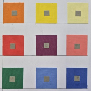 Neun unterschiedlich farbige und helle Quadrate sind auf eine Seite geklebt. In der Mitte der Quadrate klebt jeweils ein kleines, graues Quadrat genau zentriert. Das graue Quadrat hat in jedem farbigen Quadrat die gleiche Größe und wirkt doch in jeder Farbzusammenstellung anders.